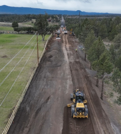Aerial view of road work on a rural road lined with trees and power lines